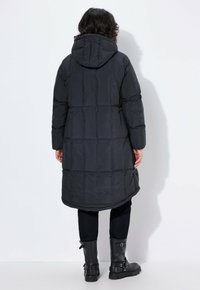 Svart pufferjacka med huva, quiltad design, lång modell och sidofickor. Matchas med mörka jeans och svarta stövlar till mitten av vaden.