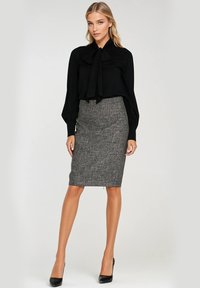 Czarna bluzka z kokardą, w połączeniu z dopasowaną szaro-skalną spódnicą o subtelnej kratkowanej strukturze. Całość dopełniają czarne szpilki w szpic.