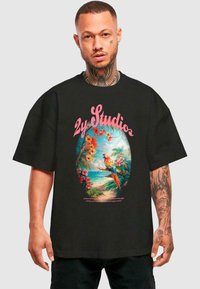 Melna oversized T-krekls ar krāsainu tropisko grafiku, kurā redzami papagaiļi, ziedi un retro stilā veidots "2y Studios" teksts.