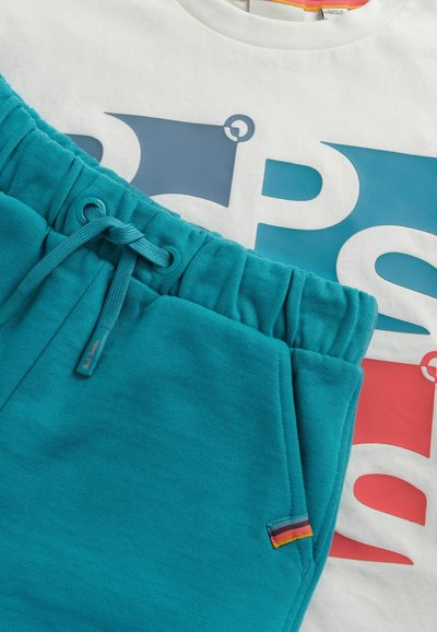 Tyrkysové tepláky s elastickým pasem a šňůrkou, doplněné bílým tričkem s velkým modrým a červeným grafickým designem.