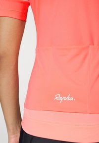 Kortermet sykkeltrøye i livlig korall, laget av fukttransporterende stoff. Har en baklomme og «Rapha.»-logo i hvitt.