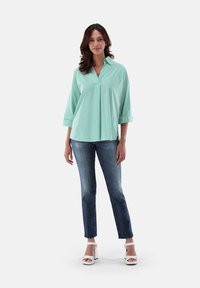 Mint green striped blouse with three-quarter sleeves, loose fit, and collar, paired with light blue jeans and white block-heeled sandals.