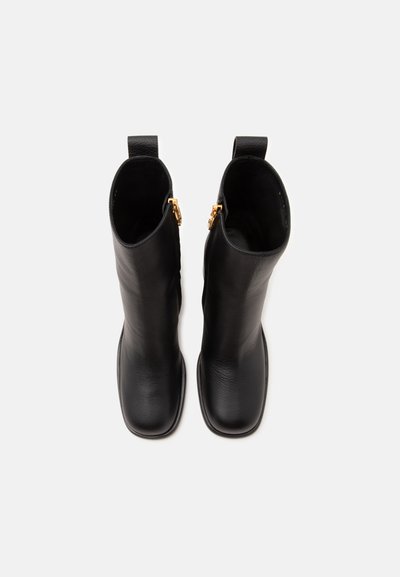Paire de bottes mi-mollet en cuir noir avec bouts carrés et fermetures éclair latérales dorées, vues de dessus sur fond blanc.