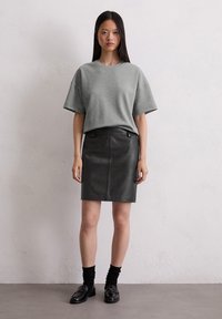 Gray oversized t-shirt and black leather pencil skirt. The fabric is smooth; the t-shirt has short sleeves and a relaxed fit. Black loafers worn with black socks.