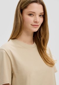 Beige, T-shirt met korte mouwen en een ronde hals, gemaakt van een zachte stof. Heeft een relaxte pasvorm en een soepele textuur.