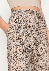 Pantalon léger à motif abstrait multicolore comprenant des teintes beige, noir et marron. Il est doté de poches latérales et d'une taille à cordon de serrage.