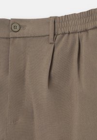Détail de la ceinture d'un pantalon marron avec fermeture par bouton, passant de ceinture, dos élastique et piqûres sur le pli avant.