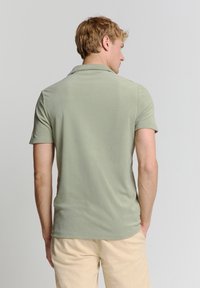 Lichtgroen poloshirt gemaakt van zacht materiaal, met een klassieke kraag en korte mouwen, weergegeven vanaf de achterzijde zonder zichtbare patronen.