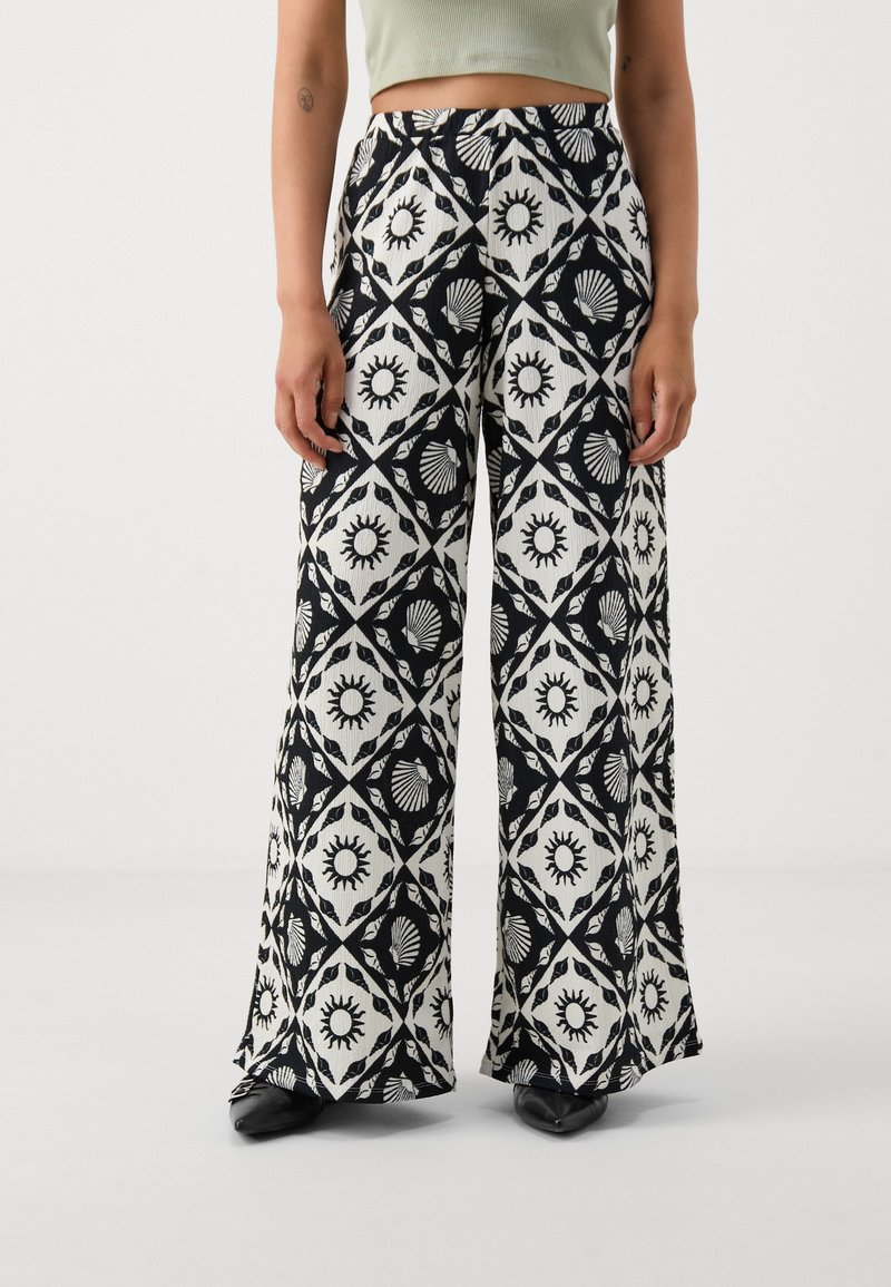 Wide-leg trousers in black and white fabric, featuring a geometric pattern with sun and shell motifs. Elastic waistband for comfort.