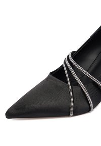 Czarny szpilka z ostrym noskiem, ozdobiona trzema błyszczącymi paskami z kryształków przechodzącymi przez stopę.