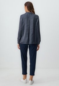 Blusa a maniche lunghe a righe navy con una trama liscia, dettaglio a pieghe sul retro e colletto, abbinata a pantaloni slim navy e sneakers bianche.