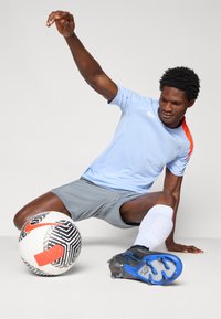 Light blue athletic shirt with red accents, gray shorts, black and blue cleats, and a black-and-white patterned soccer ball.