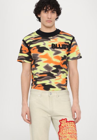 Brightly patterned short-sleeve shirt in orange, green, and black with a "BLUE" patch. Paired with light beige pants featuring bold red graphics.