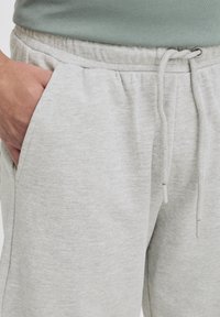 Jasnoszare dresy wykonane z miękkiej mieszanki bawełny, z elastycznym pasem i sznurkiem, bocznymi kieszeniami oraz subtelną fakturą.