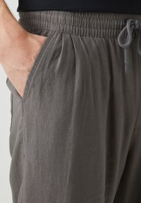 Pantalones grises y ligeros con una cinturilla elástica y cordón, bolsillos laterales y un corte holgado con pliegues sutiles.