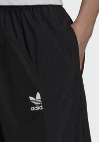 Svarta träningsbyxor i lätt, strukturerat material, med en vit Adidas-logotyp och sidofickor. Elastisk midja.