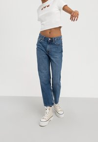 Light blue denim jeans with a straight cut and frayed hem, paired with a white cropped top featuring butterfly embroidery.