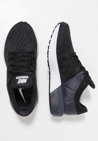 Scarpe da corsa Nike nere con una tomaia in maglia testurizzata, suole bianche e accenti scuri. Presentano lacci e un colletto imbottito per il supporto.