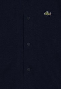 Cardigan a maglia blu navy con una finitura testurizzata, caratterizzato da bottoni davanti e un piccolo logo ricamato a forma di coccodrillo sul lato sinistro.