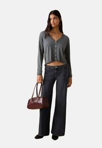 Cardigan gri scurt cu nasturi, blugi încolăciți în talie înaltă, de culoare închisă, și o geantă de mână burgundă. Prezintă o croială lejeră și o siluetă cu picioare largi.