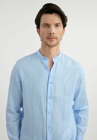 Jasnoniebieska koszula z długim rękawem, wykonana z lnu, z kołnierzykiem mandaryńskim i zapięciem na guziki, z małym haftowanym logo na piersi.