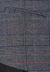 Szaro-granatowa tkanina w kratę o teksturowanym splocie, z czerwonymi akcentującymi paskami. Zawiera kieszeń naszywaną, szczegółowy wzór oraz gładkie wykończenie.