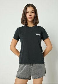 Must tatt, millel lühikeste varrukatega särk, mis on valmistatud puuvillast, millel on rinna peal väike valge logo ja mugav lõige. Kombineeritud hallide tekstuuriga lühikeste pükstega.