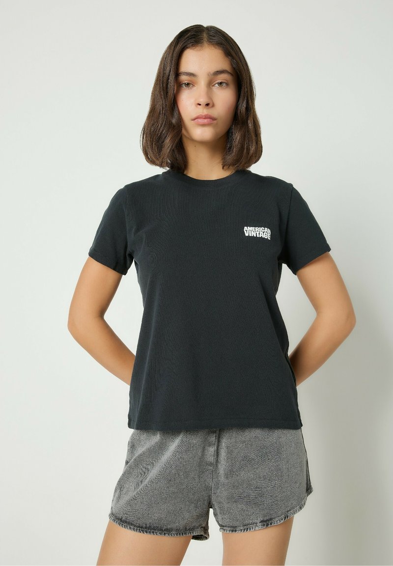 Mustavartaloinen lyhytnokkainen t-paita, joka on valmistettu puuvillasta. Paidassa on pieni valkoinen logo rinnassa ja rento malli. Yhdistettynä harmaisiin tekstuurikuvioisiin shortseihin.