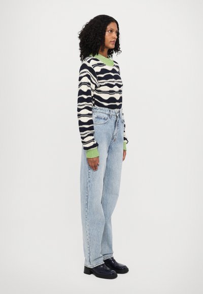Maglione lavorato a maglia con motivo ondulato blu navy e panna, polsini a coste verdi; jeans chiari a vita alta; scarpe con plateau nere.