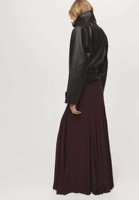 Czarna skórzana kurtka z wysokim kołnierzem, noszona na zwiewnej bordowej spódnicy maxi, eksponująca gładką fakturę i warstwowy fason.