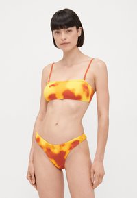 Ribbede bikini-set i oransk og gult med abstrakte mønstre. Toppen har tynne stropper og et bandeau-design; bunnen er en lavt skåret bikinitruse.