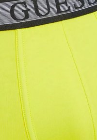 Boxers jaunes néon avec une large ceinture élastique noire ornée du logo "GUESS" en gris et des détails de couture visibles. Tissu doux et extensible.
