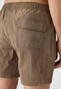 Bruine zwemboxers met een subtiel ruitpatroon, elastische tailleband en een achterzak met een messing oogletdetail. Lichtgewicht stof.