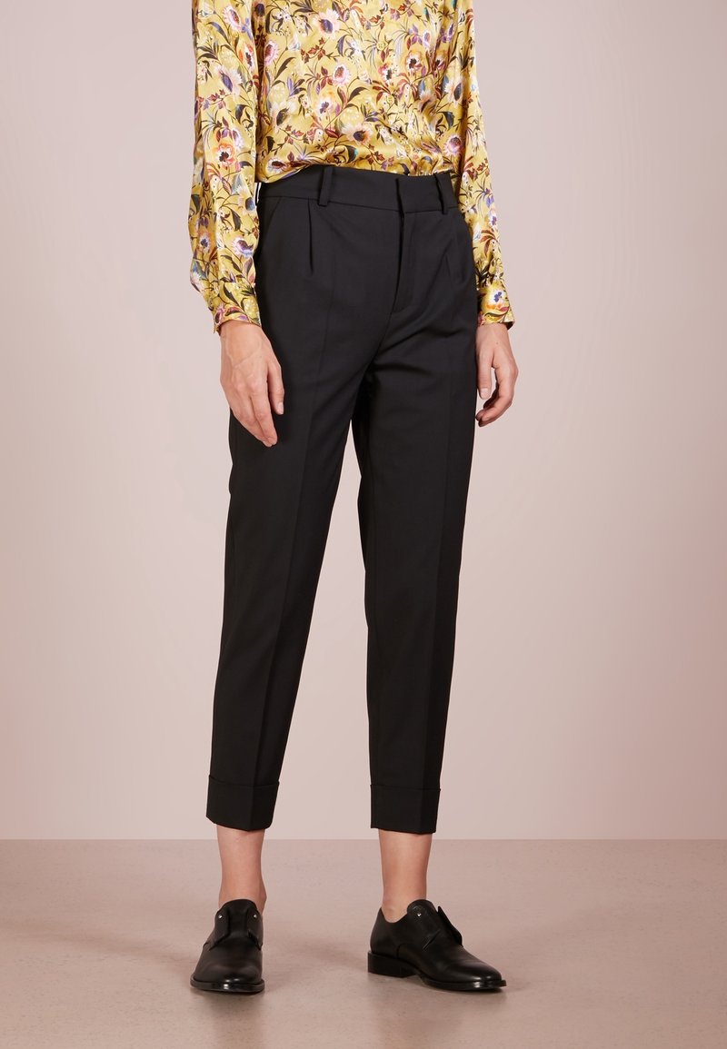 Černé kalhoty na míru s rovným střihem, s manžetovými lemy a hladkou texturou, v kombinaci s puntíkovanou žlutou blůzou.