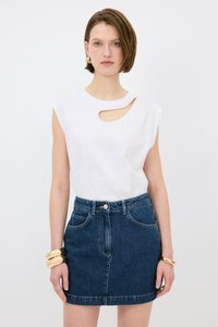Biała bluzka bez rękawów z wycięciem po boku i złotym akcentem w postaci łańcuszka, w połączeniu z ciemnoniebieską spódnicą dżinsową o dopasowanej talii i kieszeniach.