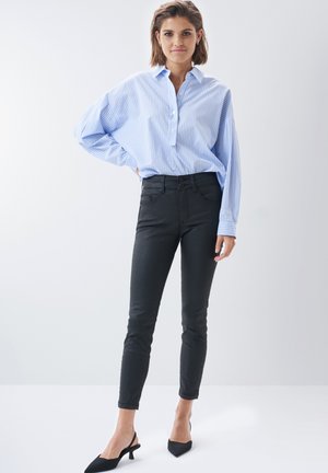 Chemise boutonnée rayée bleu clair, jeans skinny noirs et sandales à talons ouverts noires. Manches détendues et coupe décontractée.