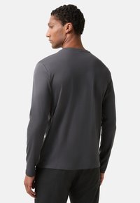 Šedá dlouhá rukávová košile vyrobená z měkkého materiálu, s jednoduchým designem a kulatým výstřihem. Zadní strana má hladkou strukturu bez viditelných vzorů.