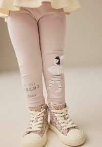 Leggings rosa chiaro con un design stampato di un artista di circo e testo. Abbinati a sneakers alte scintillanti e multicolori.
