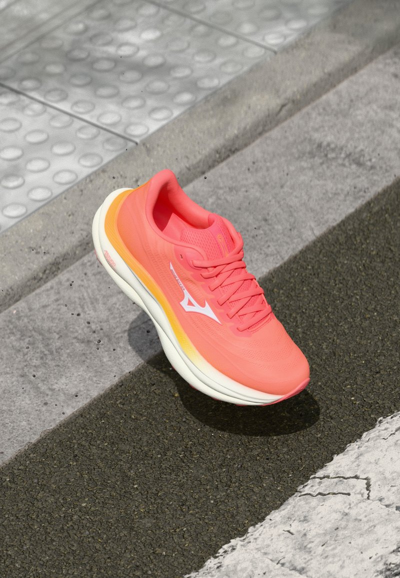 Shoe de corrida rosa com um upper de malha leve, detalhes brancos e uma sola ligeiramente texturizada com um degradê de rosa a laranja.