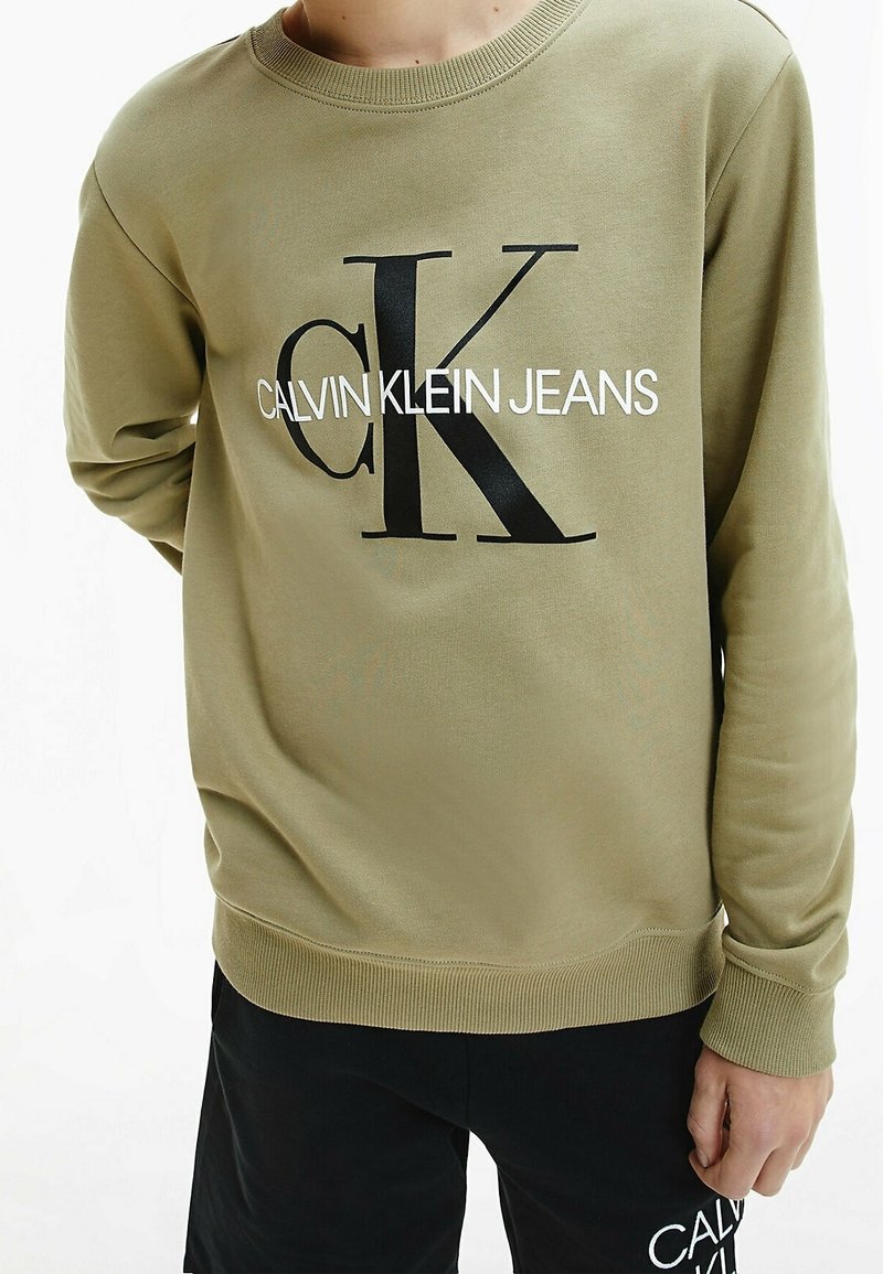 Oliwkowy sweter z bawełny, z dużym czarnym nadrukiem logo "CK" oraz białym napisem "CALVIN KLEIN JEANS" poniżej. Ściśnięte mankiety i dół.