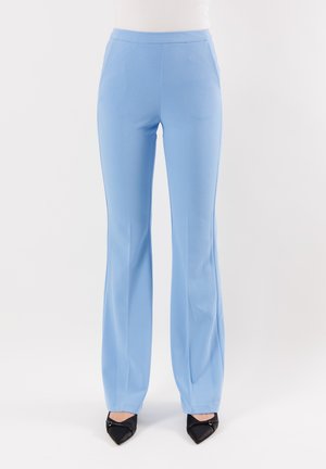 Pantaloni aderenti di colore azzurro chiaro con una texture liscia, silhouette svasata e dettagli di piega discreti. Abbinati a scarpe con tacco a punta nere.