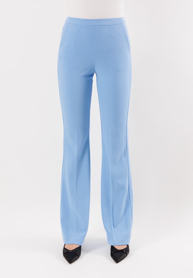 Pantaloni aderenti di colore azzurro chiaro con una texture liscia, silhouette svasata e dettagli di piega discreti. Abbinati a scarpe con tacco a punta nere.