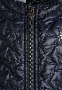 Giacca trapuntata blu navy con motivi a stella, zip centrale con tirante a forma di cuore e una texture morbida e liscia.