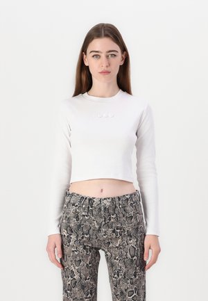 Witte langlopende cropped top met geborduurd "HUGO" logo, gecombineerd met high-waisted broek met een slangenprintpatroon in grijstinten en zwart.
