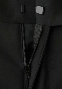 Zbliżenie czarnego materiału pokazujące częściowo odbezpieczony suwak i dwa metalowe haczyki zapięć na górnym brzegu ubrania.