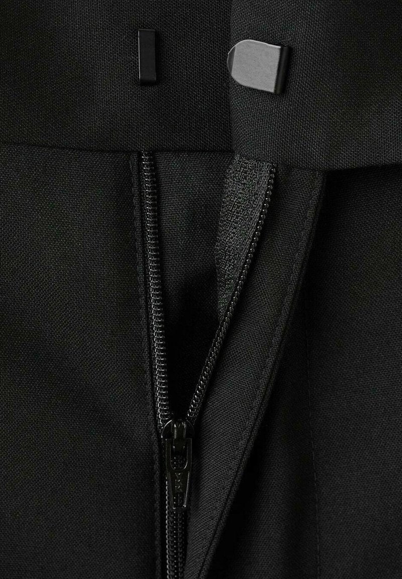 Nahaufnahme eines schwarzen Stoffes mit teilweise geöffnetem Reißverschluss und zwei Metall-Haken am oberen Rand des Kleidungsstücks.
