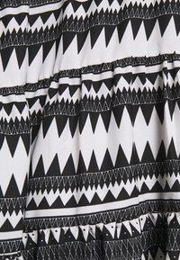 Svart- och vitt tyg med ett geometriskt mönster av trianglar och linjer, med volangtextur längs den nedre kanten.