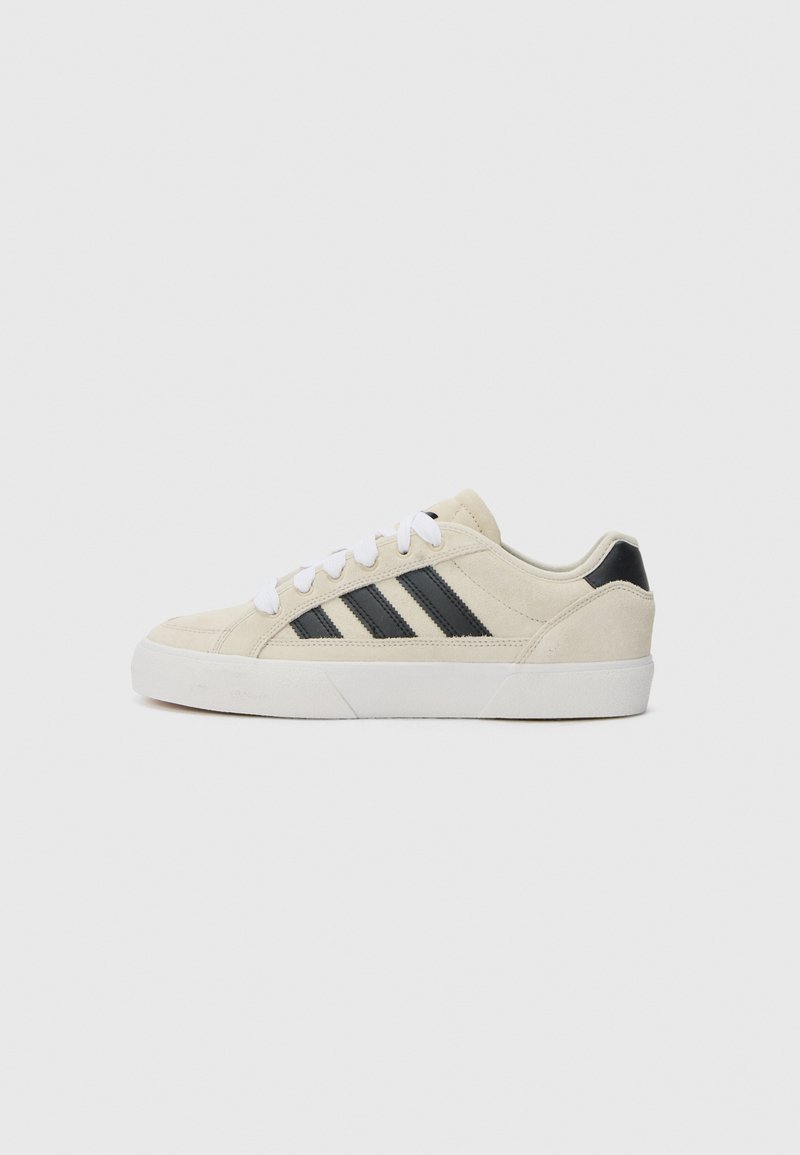 Beige semskinn sneakers med svarte striper, hvite snørebånd og en teksturert gummisåle. Lavt toppdesign med rund tå.