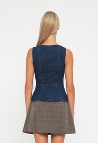 Denim peplum top in donkerblauw met aansluitende lijfje en uitlopende zoom, gecombineerd met een bruine geruite skaterrok. Strakke lijnen en naadloos ontwerp.
