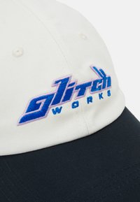 Bílá bavlněná baseballová čepice s námořnickým kšiltem, vyšívané logo "glitch WORKS" s modrými a růžovými akcenty.